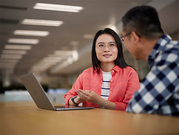 พนักงาน Apple ฝ่ายซอฟต์แวร์และบริการ 2 คนกำลังนั่งสนทนากันเรื่องงานและใช้ MacBook