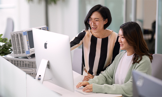 Ella ยืนข้างๆ เพื่อนร่วมงานคนหนึ่งซึ่งนั่งอยู่หน้าจอ Apple