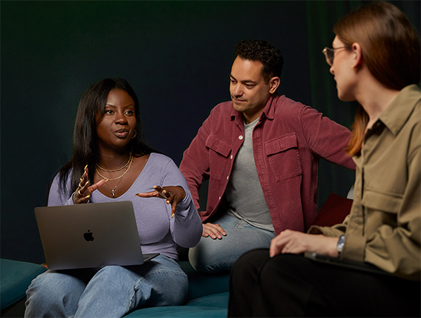 Tre persone del team Software e servizi di Apple che parlano su un divano; una con un MacBook.