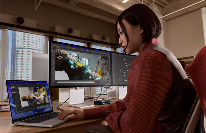 Seseorang bekerja di kantor menggunakan MacBook Pro yang terhubung ke Studio Display XDR