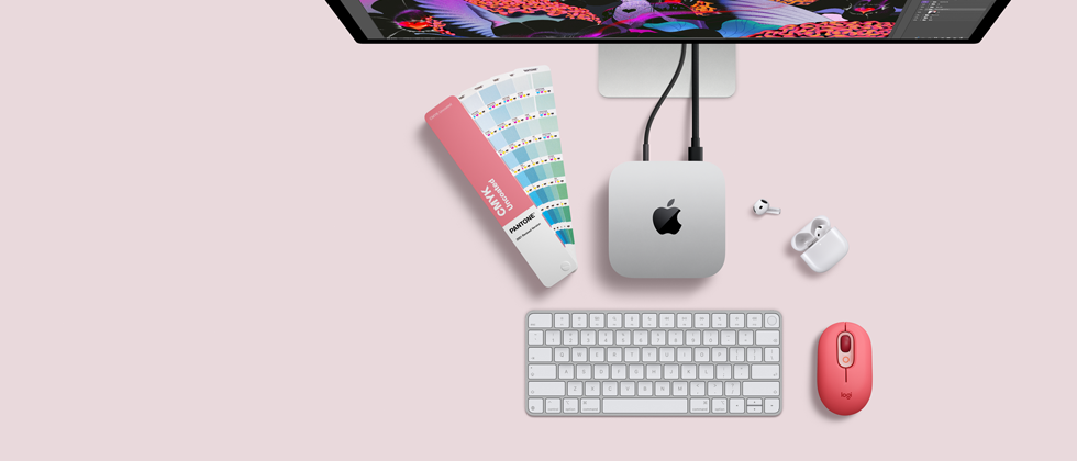 Mac mini, вид зверху, алюмінієвий корпус сріблястого кольору, заокруглені кути, глянцевий чорний логотип Apple по центру, підʼєднання за допомогою кабелю, Studio Display частково видно зверху, AirPods 4, відкриті, зразки кольорів Pantone, цифрова клавіатура та миша
