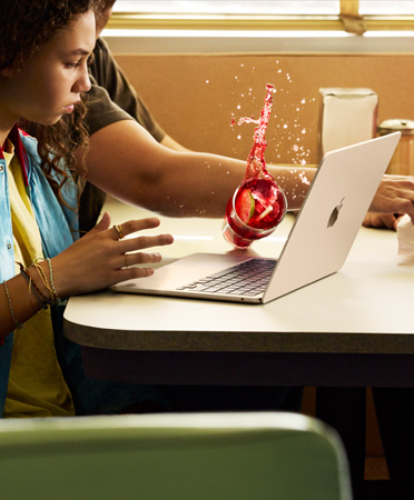 A person reaching for something in a restaurant, spilling an iced beverage over an open MacBook