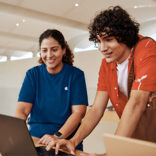 Une employée de l’Apple Store offre de l’assistance à un client devant un MacBook.