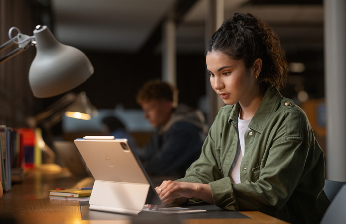 Persona che siede alla scrivania di un’aula studio e scrive su un iPad con una Magic Keyboard, dimostrando la versatilità dei dispositivi Apple