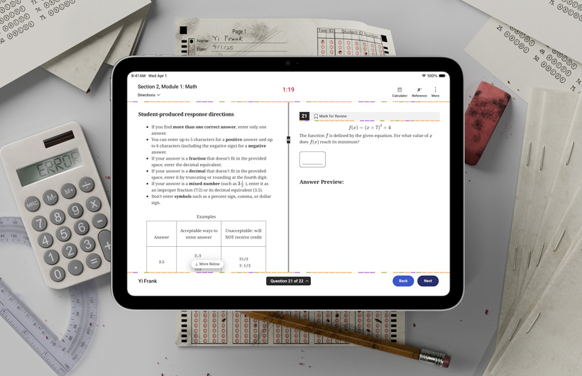 Un iPad appoggiato su una scrivania tra moduli di test cartacei e materiale scolastico. Lo schermo mostra le istruzioni per completare la parte di matematica di un test standardizzato.