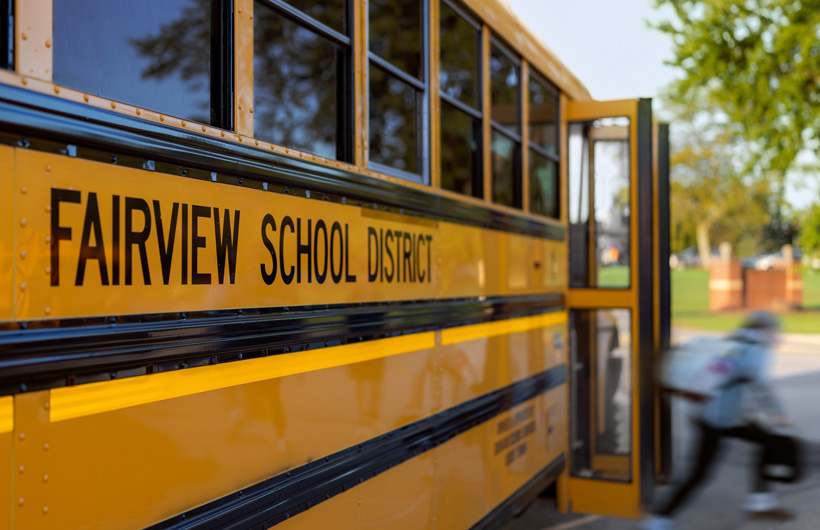 Un primo piano del lato di uno scuolabus del Fairview School District, mentre un bambino scende dall’autobus.