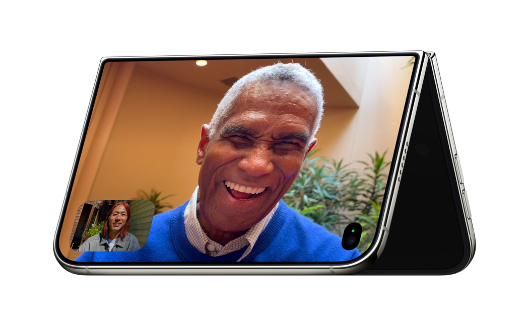 iPhone Duo, half opened, bottom panel lies flat on the surface, top and bottom displays feature two people using FaceTime