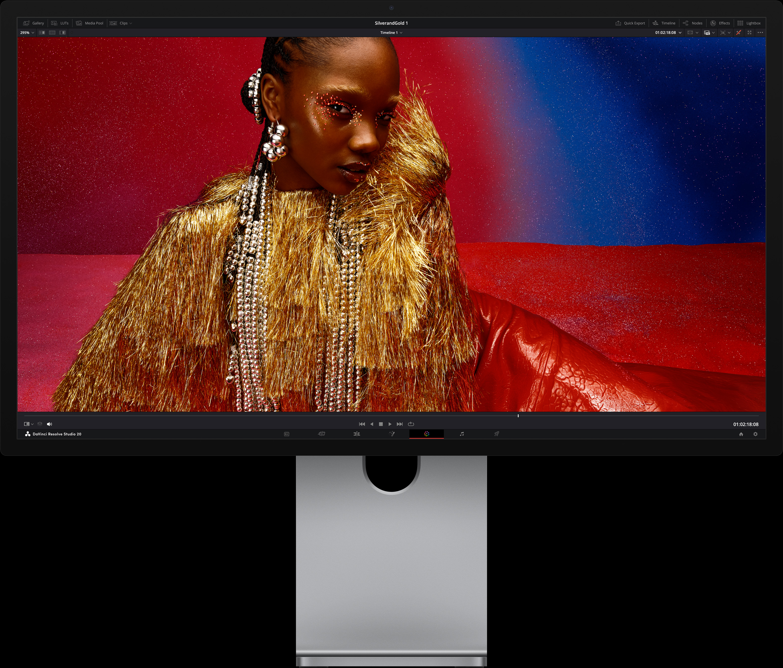 A person wearing a bright red dress and oversized metallic accessories sits in front of a blue and red gradient background, showcasing the image quality available with Studio Display XDR