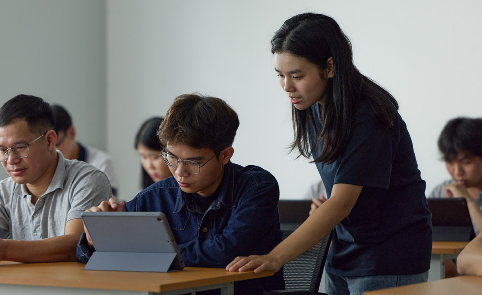 Two people in a classroom setting collaborate on an Apple tablet